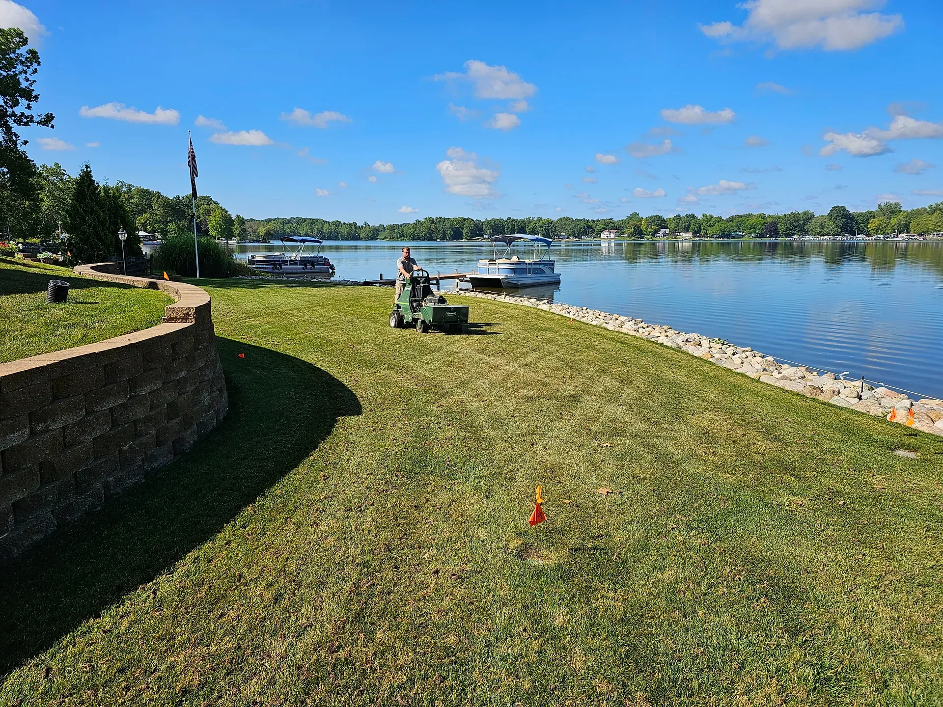 A GreenWorks technician running a core aerator across a lakeside lawn