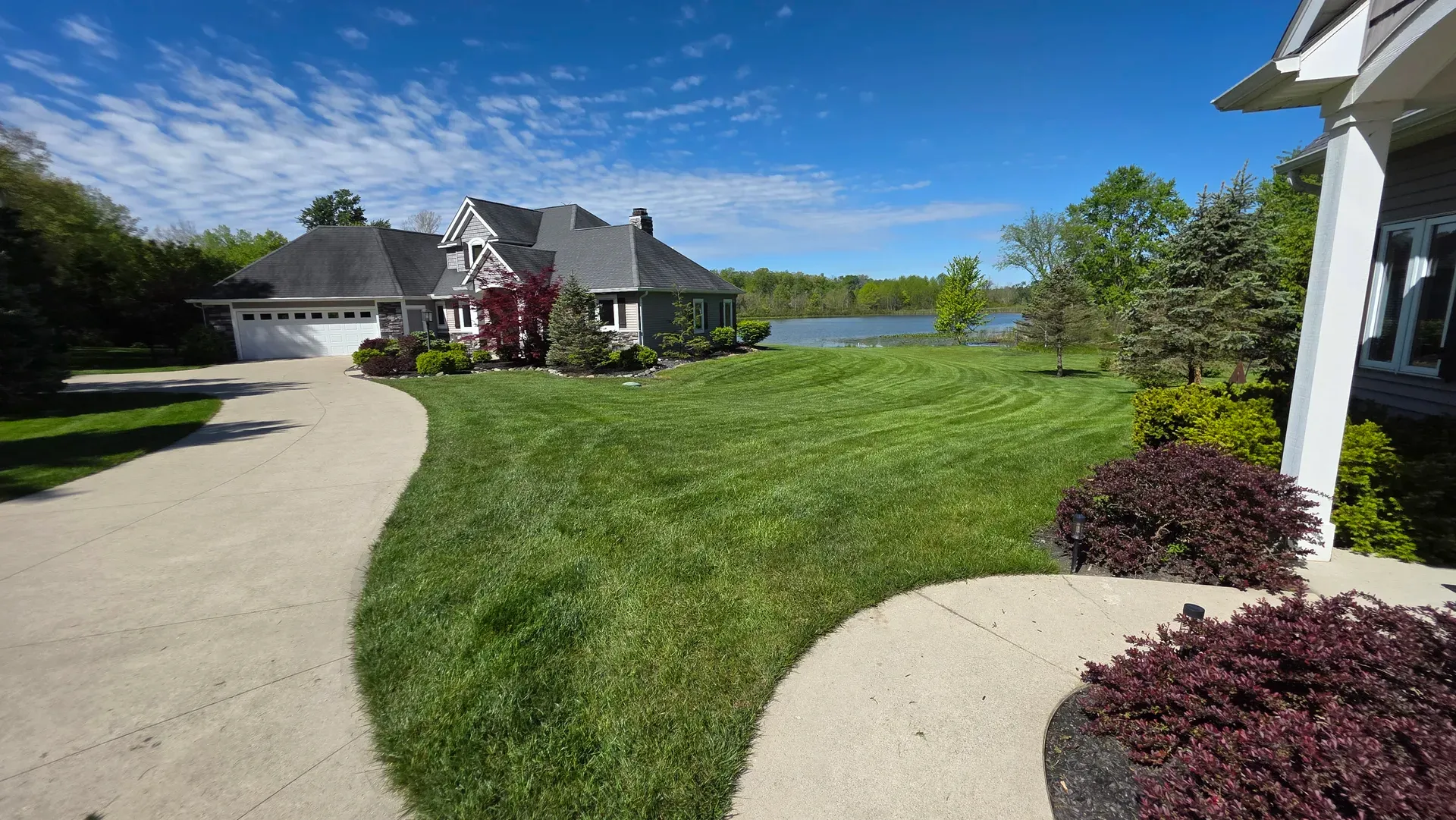 A striped lawn curving around a lakeside home under a clear sky