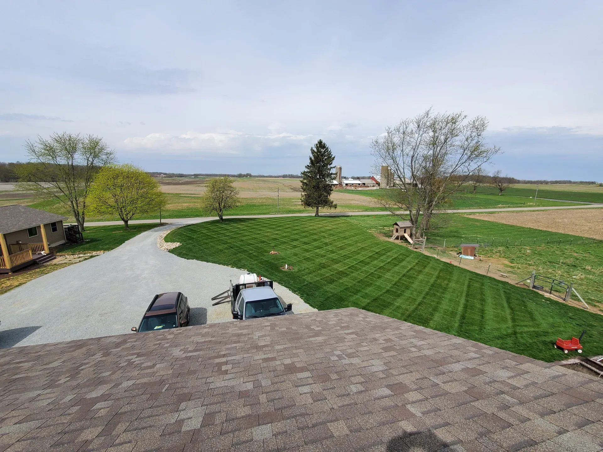 A freshly striped lawn running up to a country home with farm fields beyond