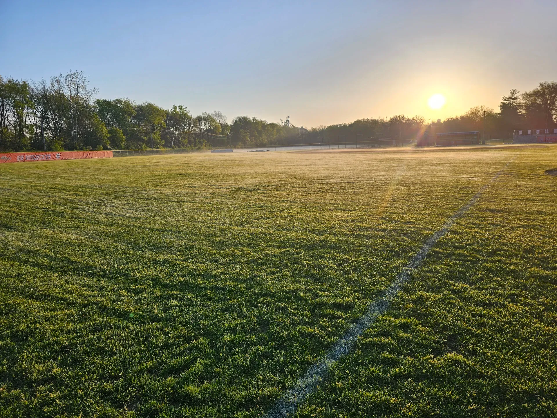 Sun rising over a striped athletic field on a misty morning